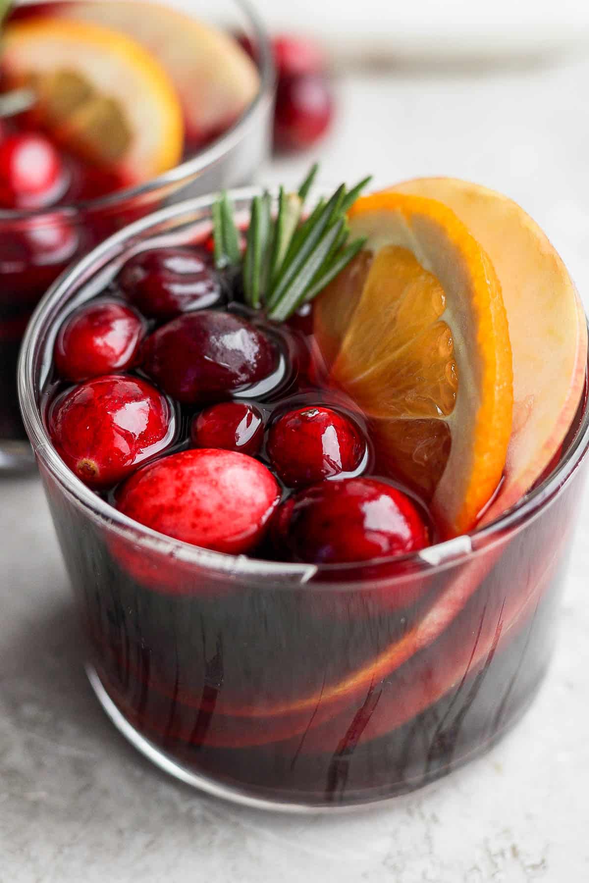 A glass of Christmas sangria garnished with cranberries, rosemary, and orange slices.