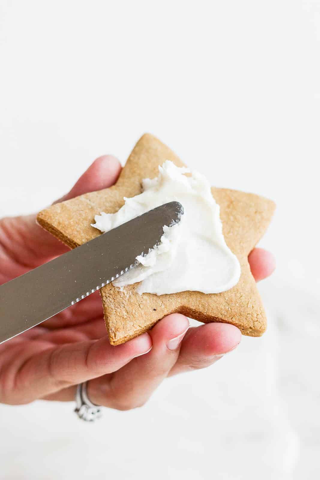 A knife putting dairy free frosting on a cut-out cookie.