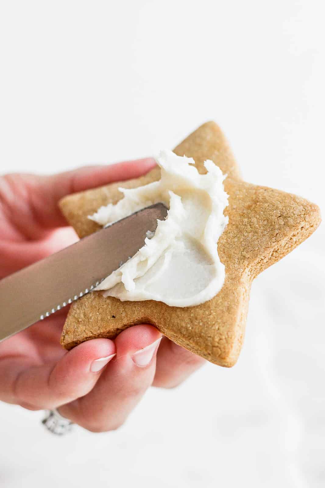 Using a knife to spread dairy free frosting on a cut-out cookie.