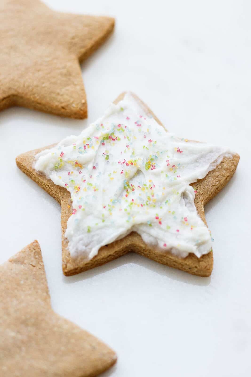 A cut-out cookie frosted with dairy free frosting and decorated with sprinkles.