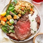 Top down shot of a plate of prime rib with horseradish sauce on top, rice pilaf and a house salad.