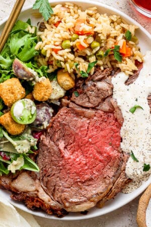 Top down shot of a plate of prime rib with horseradish sauce on top, rice pilaf and a house salad.