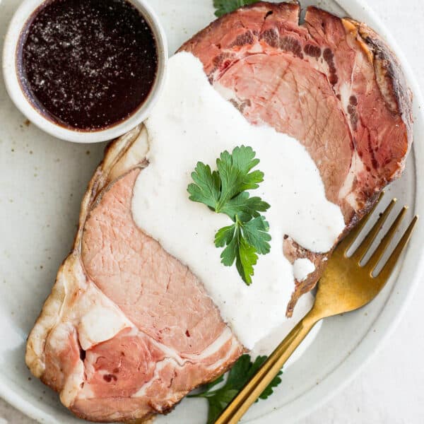 Horseradish sauce for prime rib drizzled over a piece of prime rib with au jus next to it.