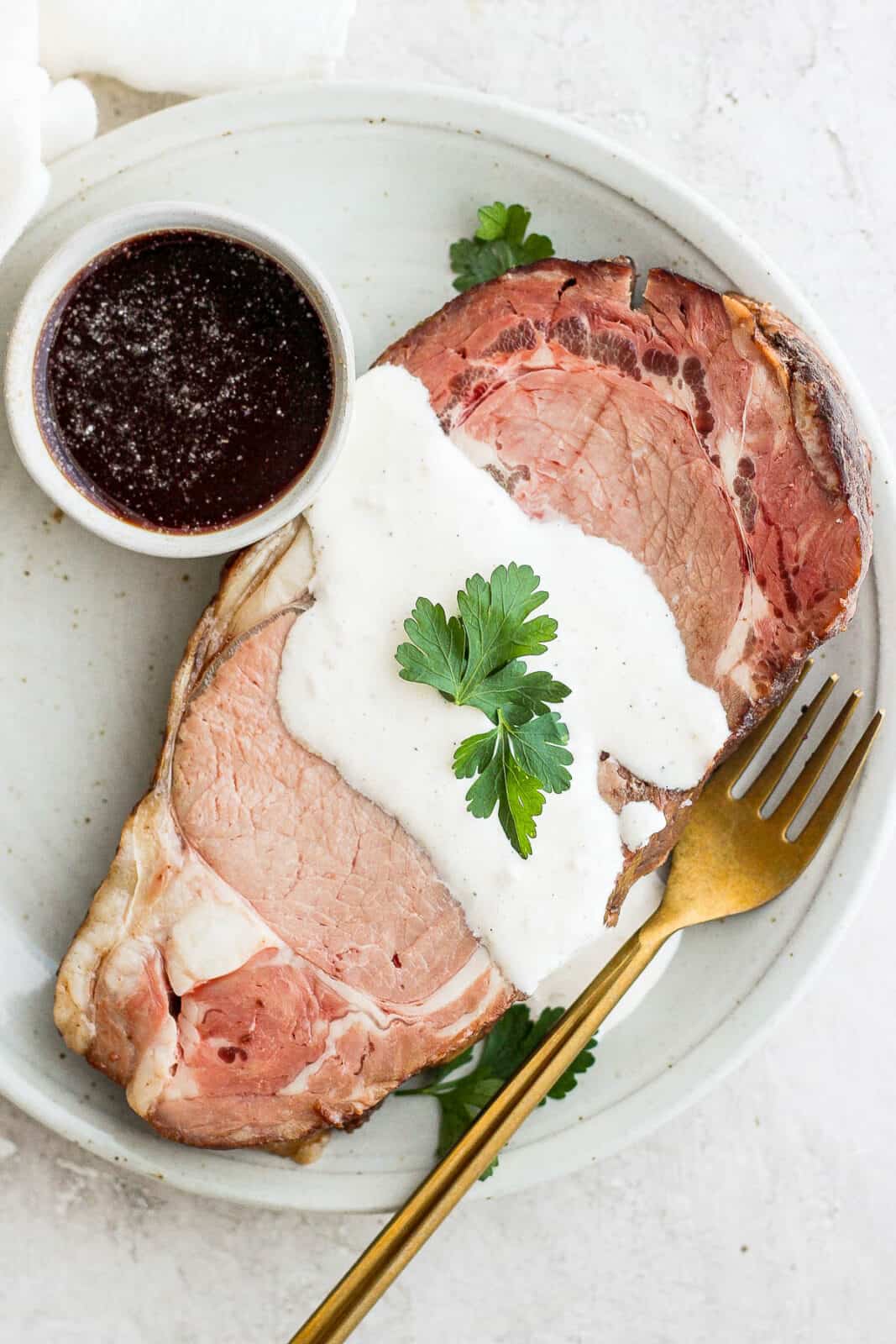 A plate with a slice of prime rib on it with horseradish sauce and a bowl of au jus. 