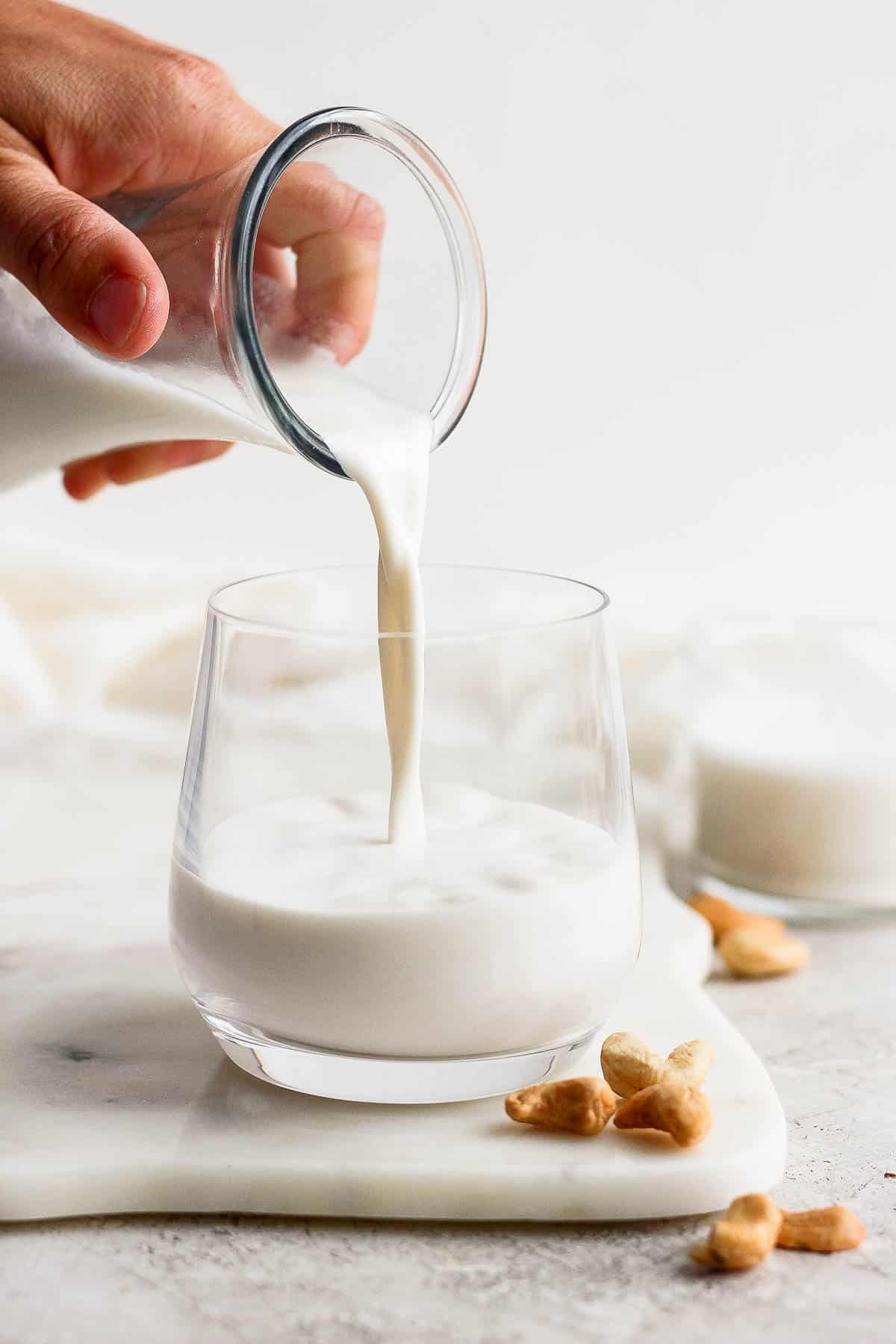 Cashew milk being poured from a carafe into a glass.