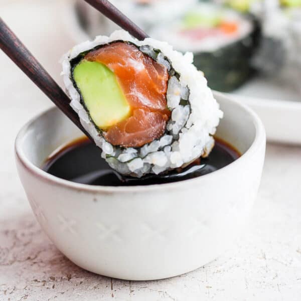 Someone dipping homemade sushi into a bowl of soy sauce.