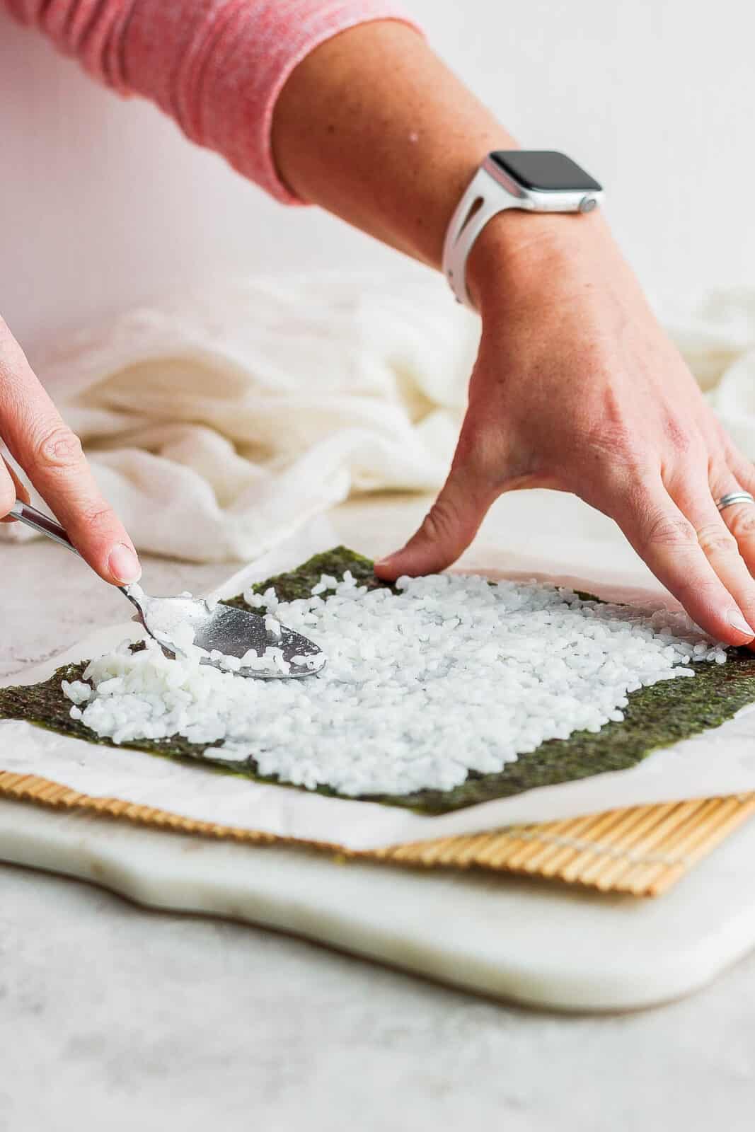 Using a spoon to spread a thin layer of rice on the nori sheet.