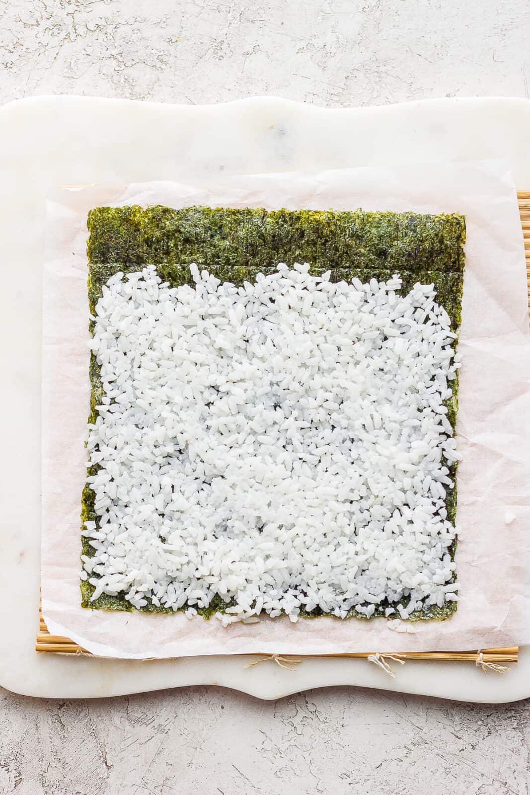 A thin layer of rice covering all but the top 1/2 inch of the nori sheet.