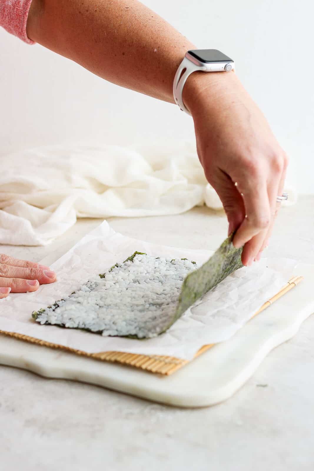 A hand lifting the top of the nori sheet to begin flipping it over.