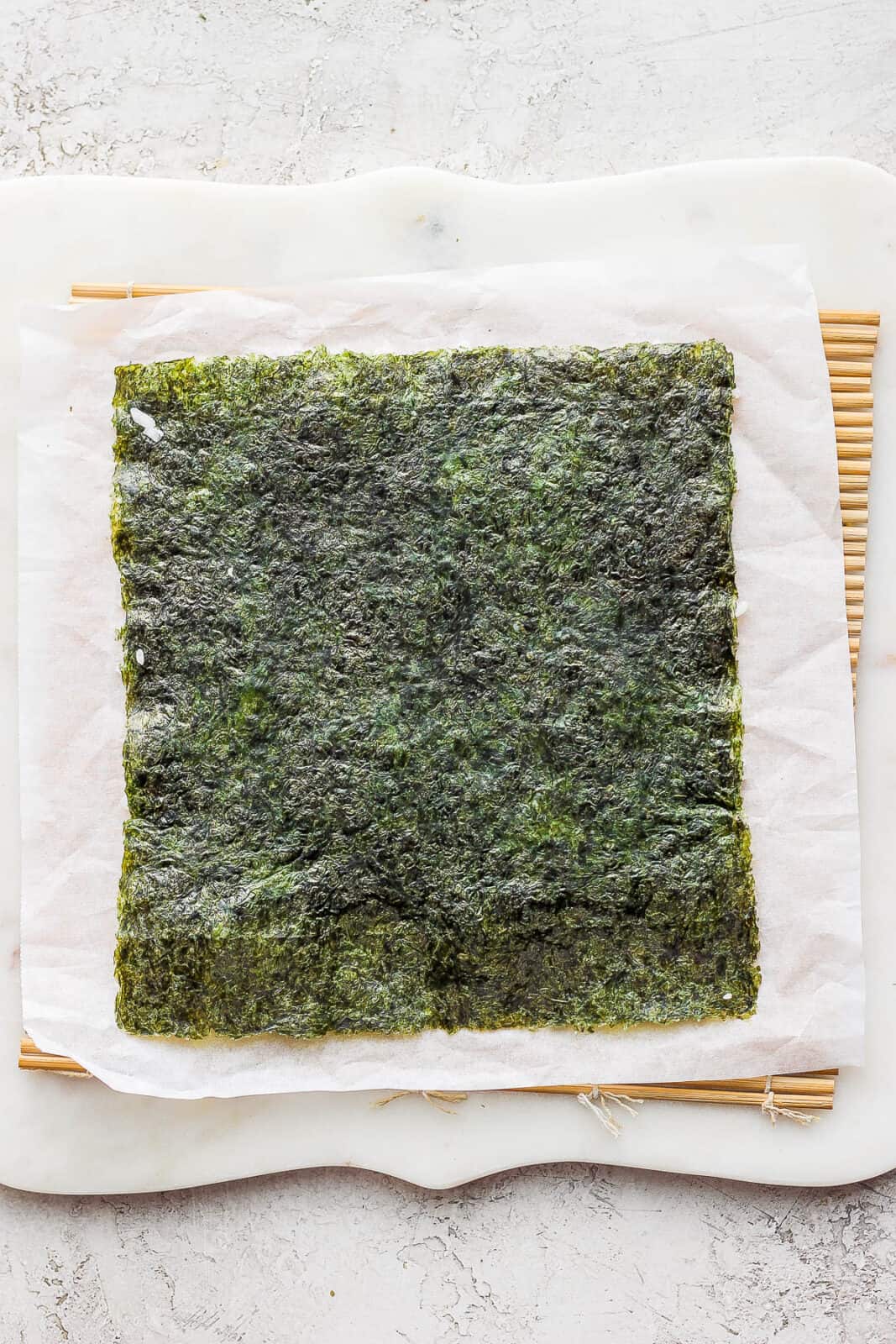 The nori sheet on top of the parchment paper with the rice-side down.