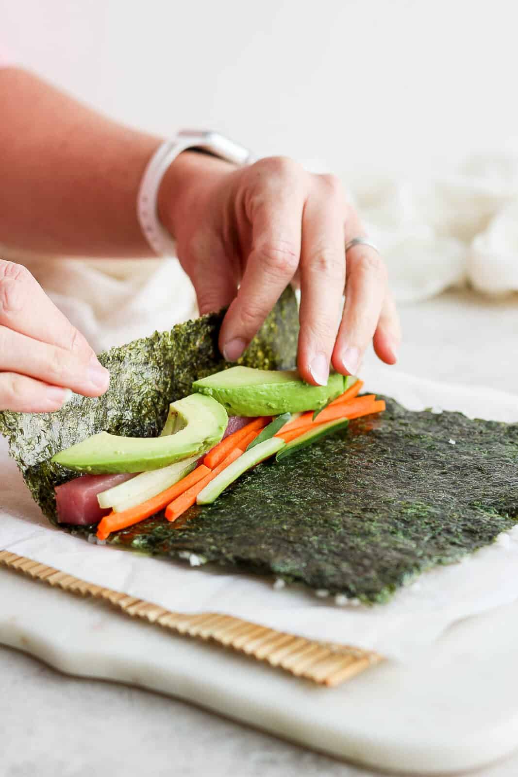 Two hands lifting the end of the nori sheet over the filling.