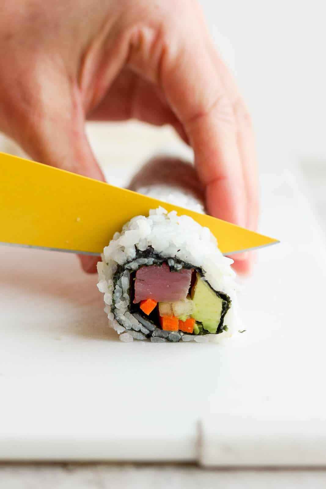 A sharp knife cutting the sushi roll into pieces.