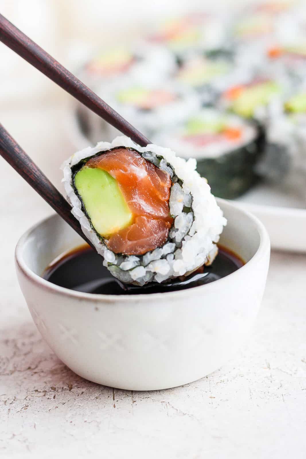 Chopsticks dipping a sushi roll in a dish of soy sauce.