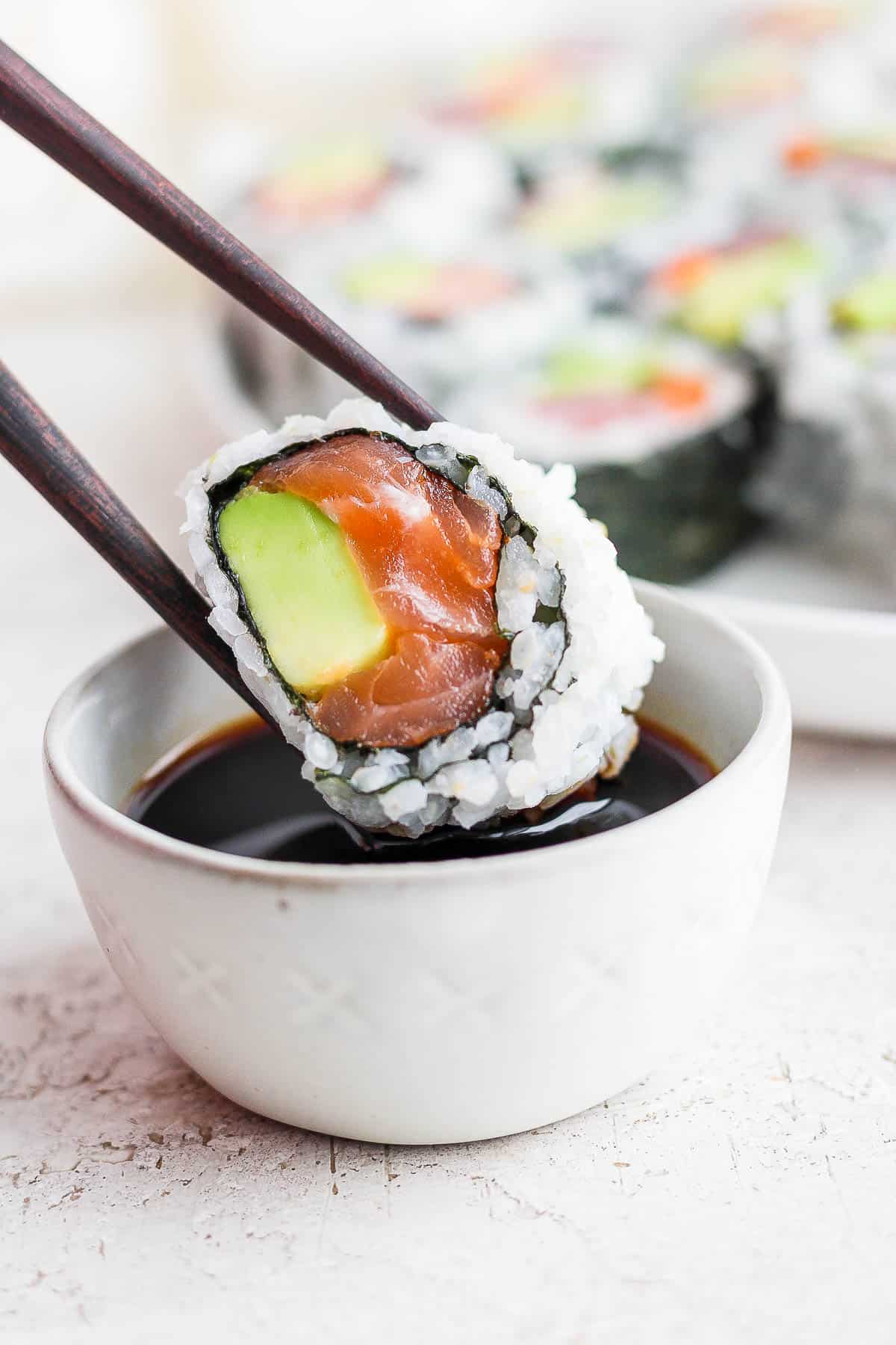 A piece of sushi being dipped in soy sauce with chopsticks.