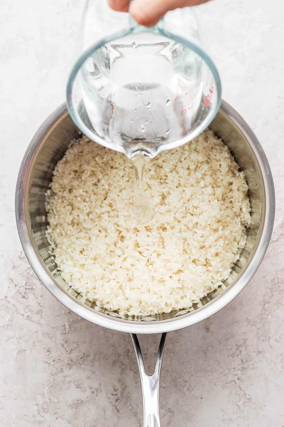 Water being poured into a pot with the rinsed sushi rice.