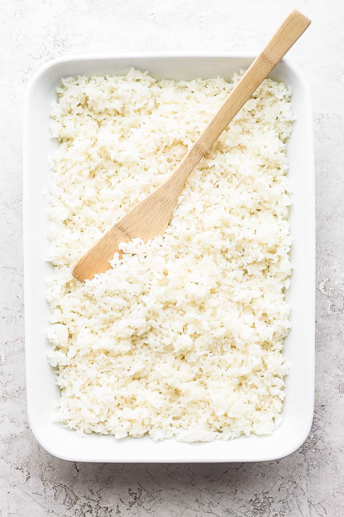 Sushi rice in a large dish with a wooden paddle.