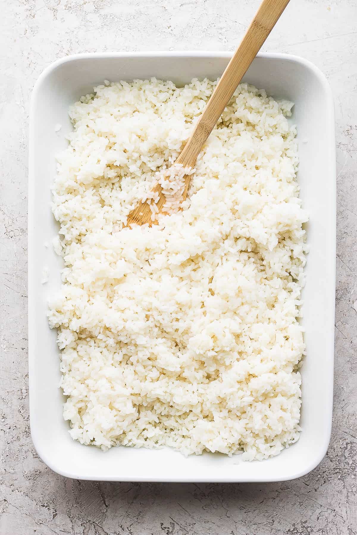 Cooked sushi rice in a dish with a wooden spoon.