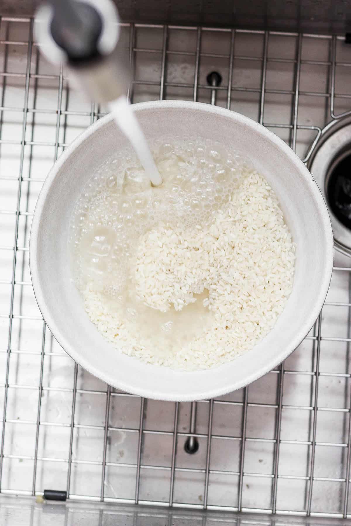 Water being poured into a bowl of sushi rice.