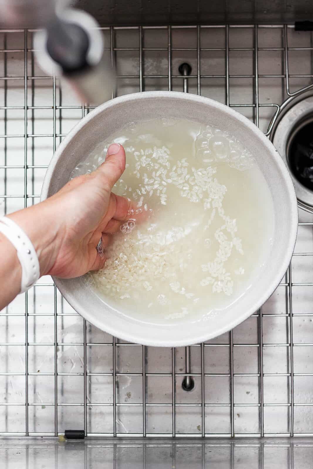 A hand mixing the rice in water.