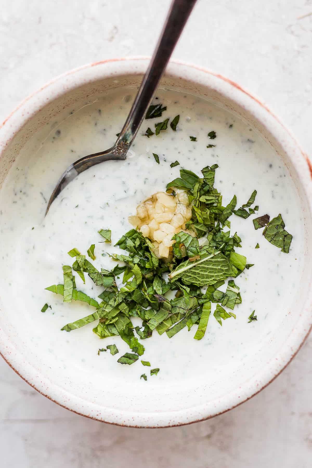 Lamb sauce in a bowl with some extra mint and garlic and a spoon sticking out the side.
