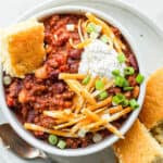 Bowl of slow cooker chili with some cheese, sour cream and corn bread.