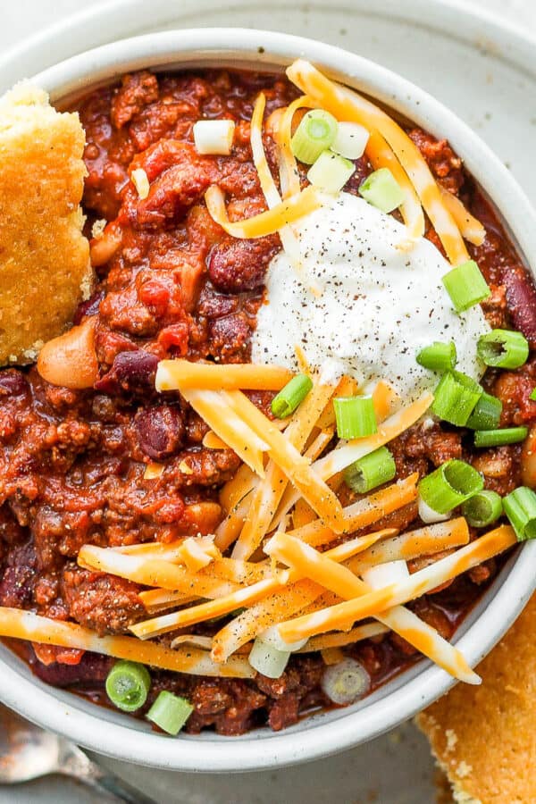 Bowl of slow cooker chili with some cheese, sour cream and corn bread.