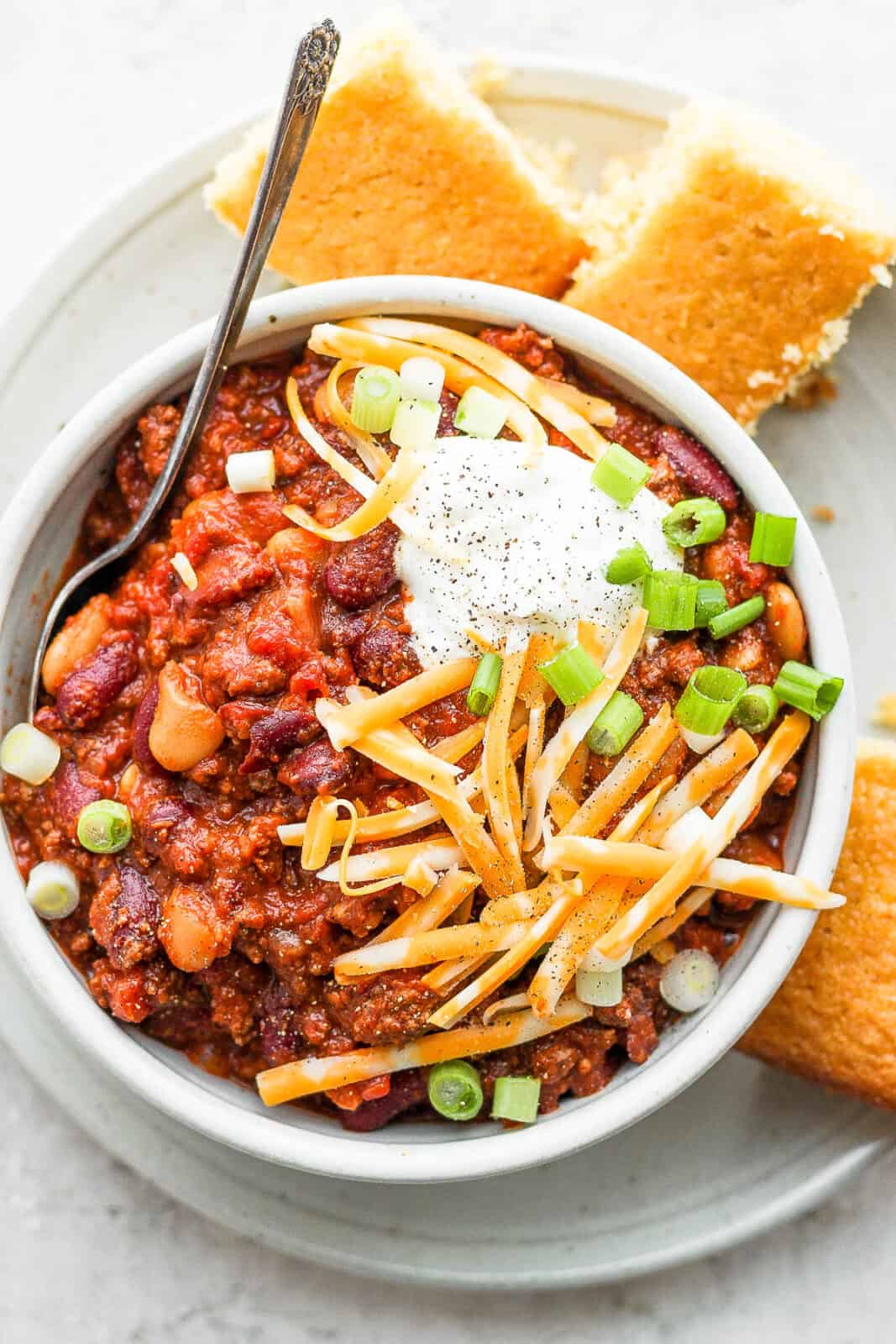A bowl of slow cooker chili with toppings and cornbread on the side.