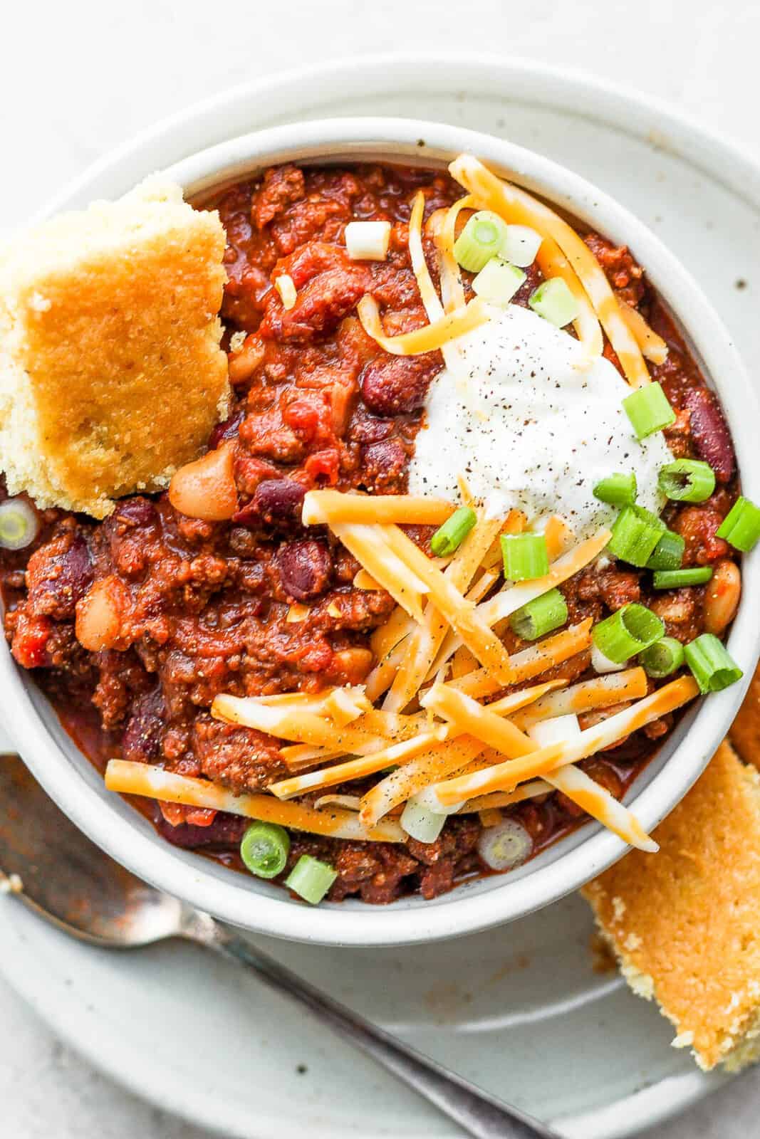 A bowl of slow cooker chili with toppings and cornbread.