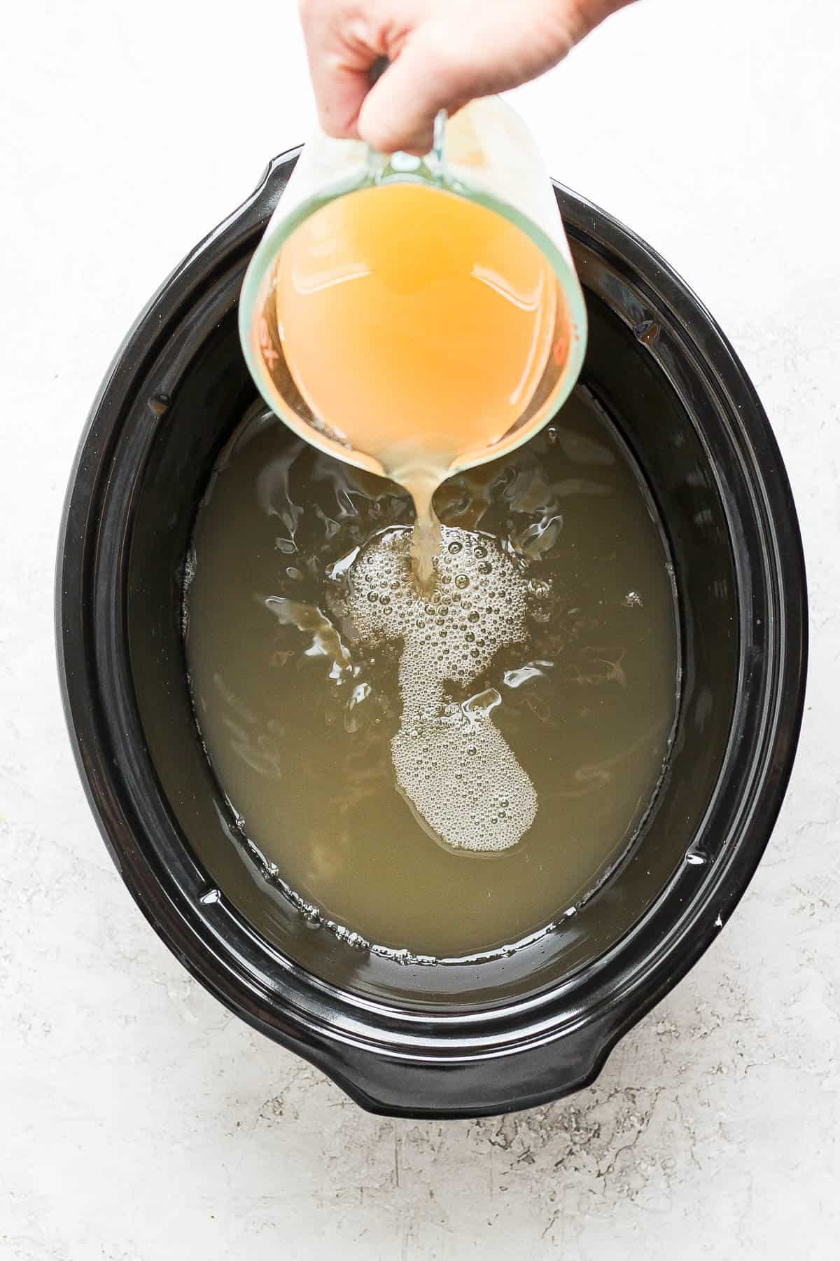 Apple cider being poured into a slow cooker.