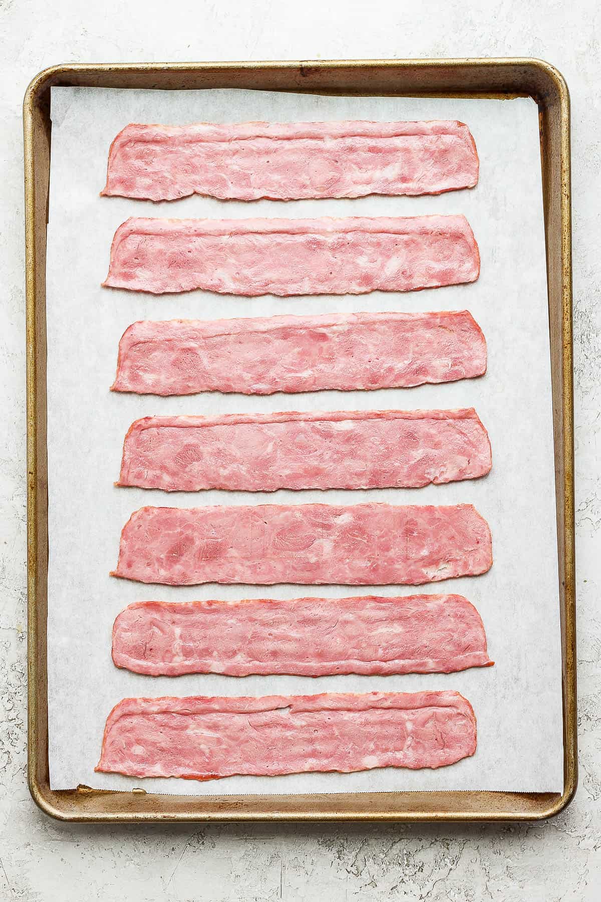 Raw bacon on a parchment-lined pan.