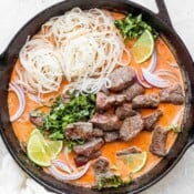 Cast iron skillet full of beef curry and rice noodles.