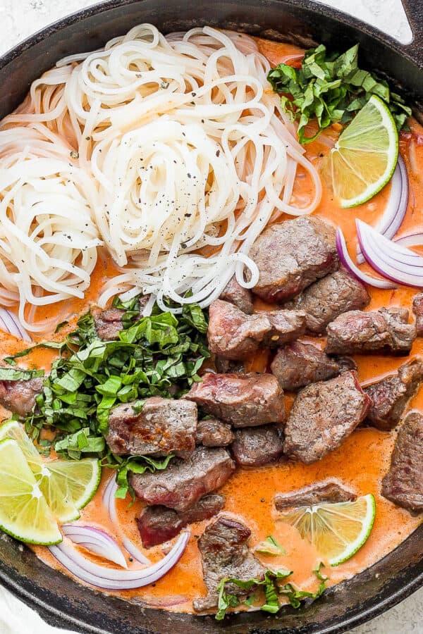 Cast iron skillet full of beef curry and rice noodles.