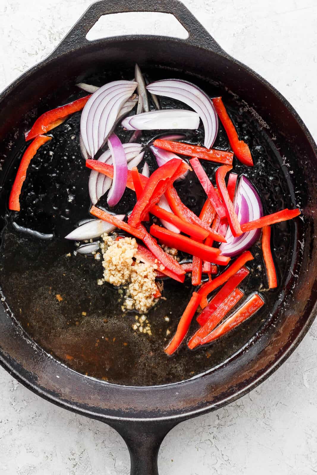 Cast iron skillet with garlic, red onion and red bell pepper inside.