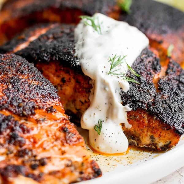 Cooked blackened salmon on a plate topped with dill sauce and fresh dill.