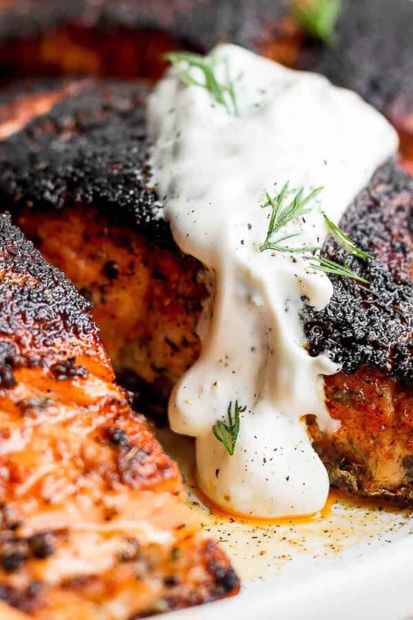 Cooked blackened salmon on a plate topped with dill sauce and fresh dill.