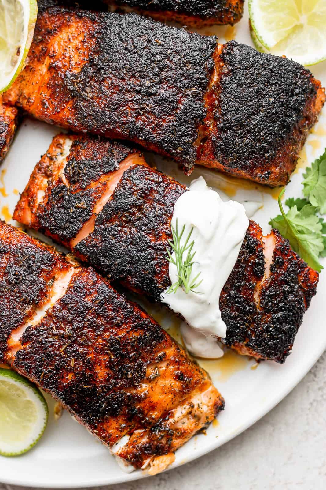 Blackened salmon fillets on a plate with dill sauce.