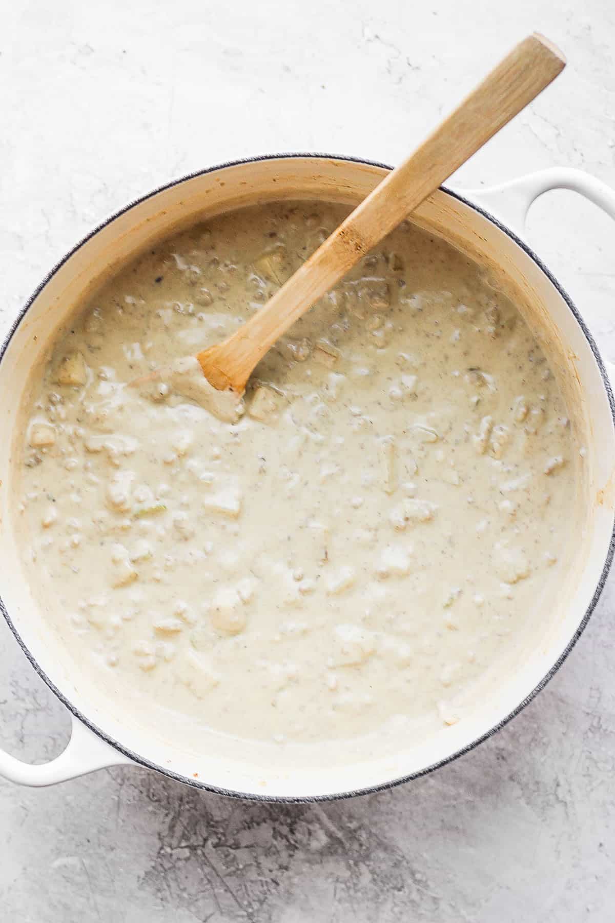 Cheeseburger soup in a dutch oven with a wooden spoon sticking out. 