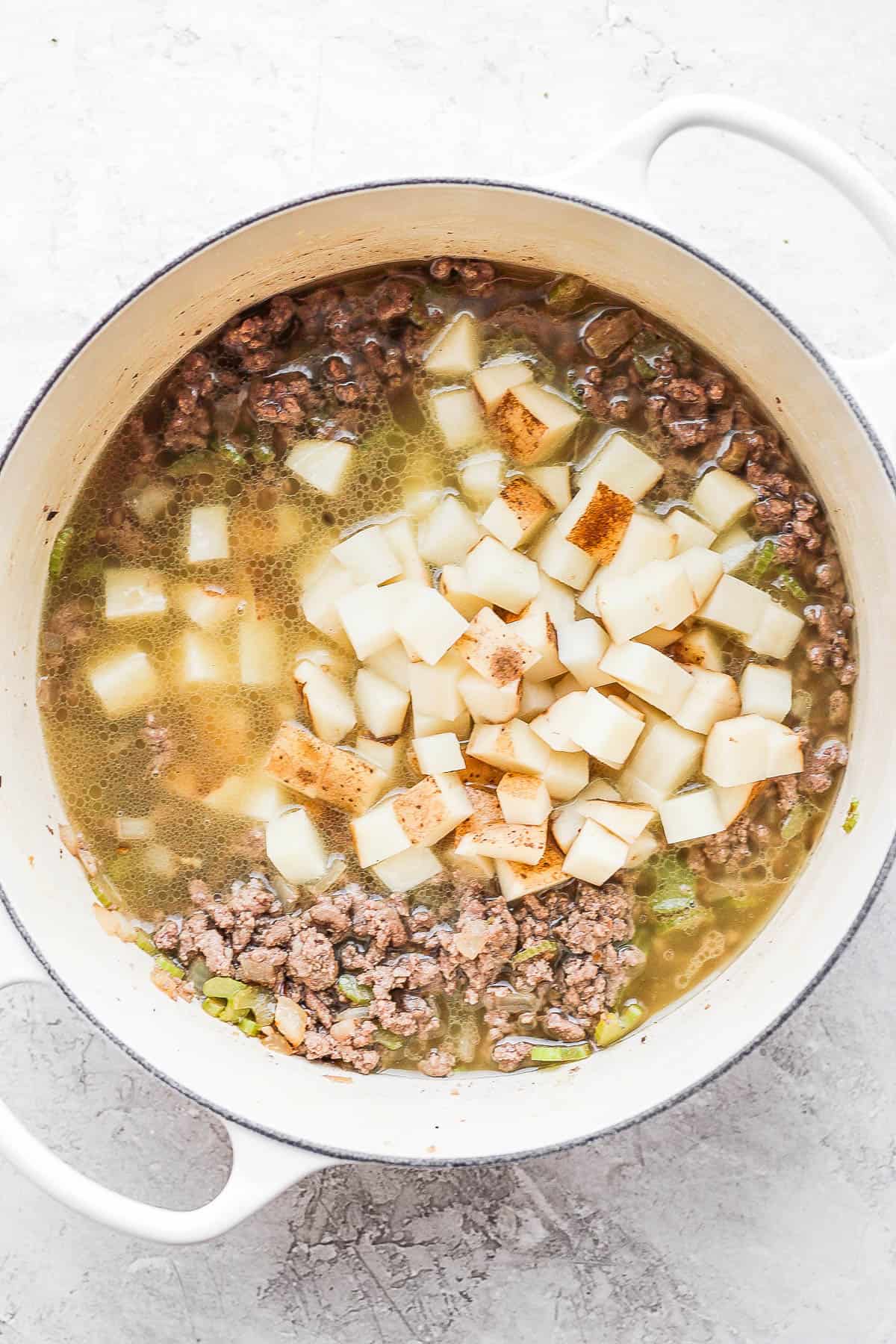 Potatoes and broth have been added to the dutch oven along with the ground beef.