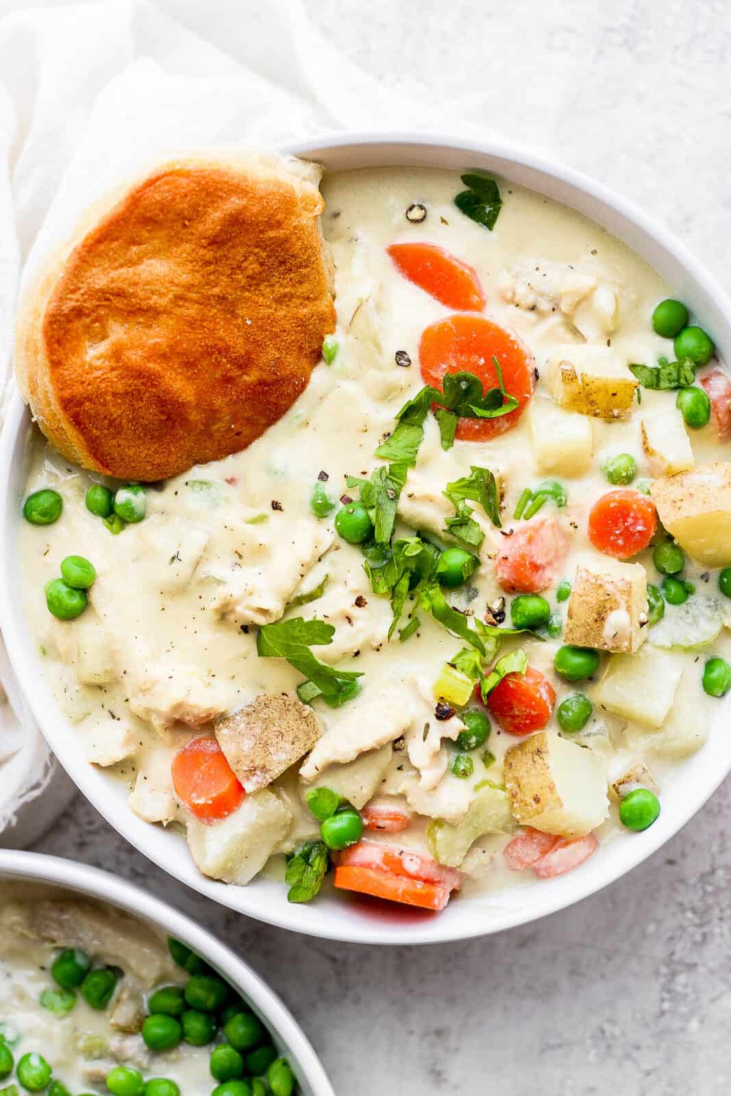 A bowl of chicken pot pie soup with a biscuit.