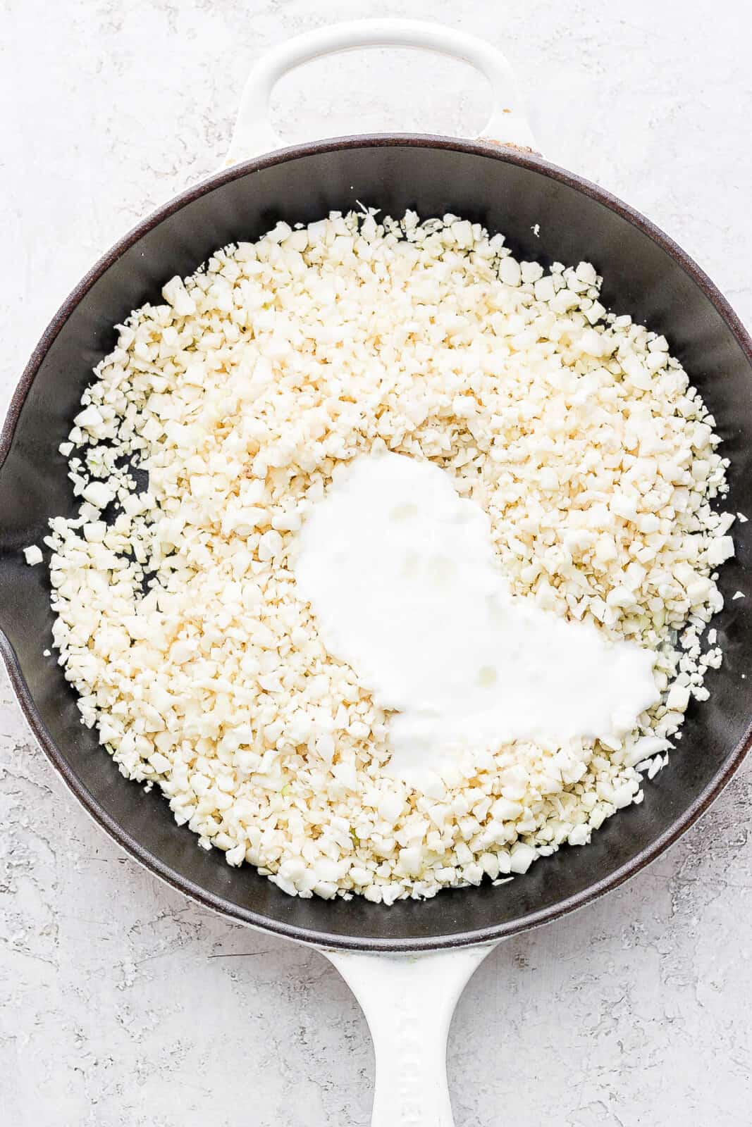 Cauliflower rice in a skillet with coconut milk added.