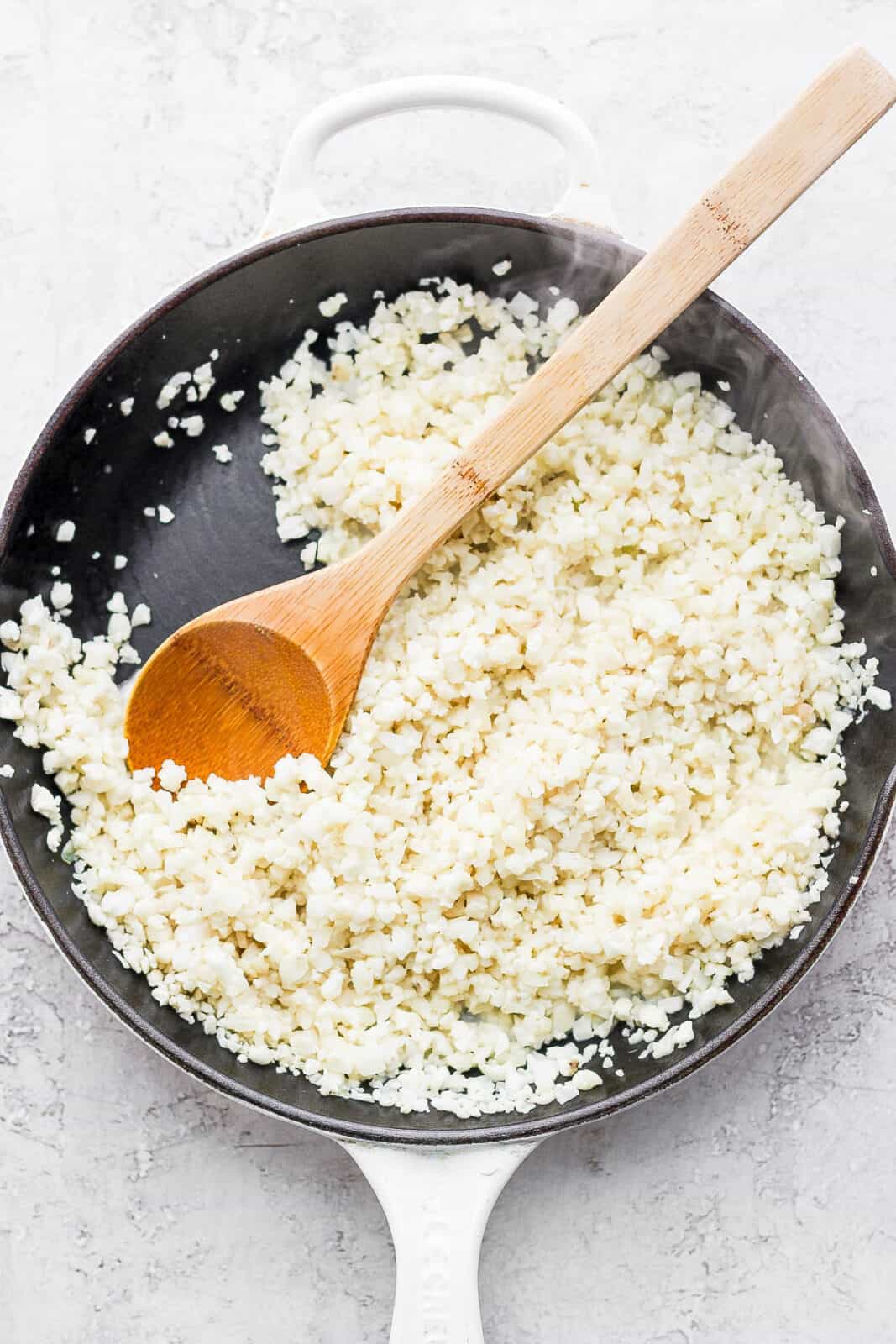 Coconut cauliflower rice in a skillet with a wooden spoon.