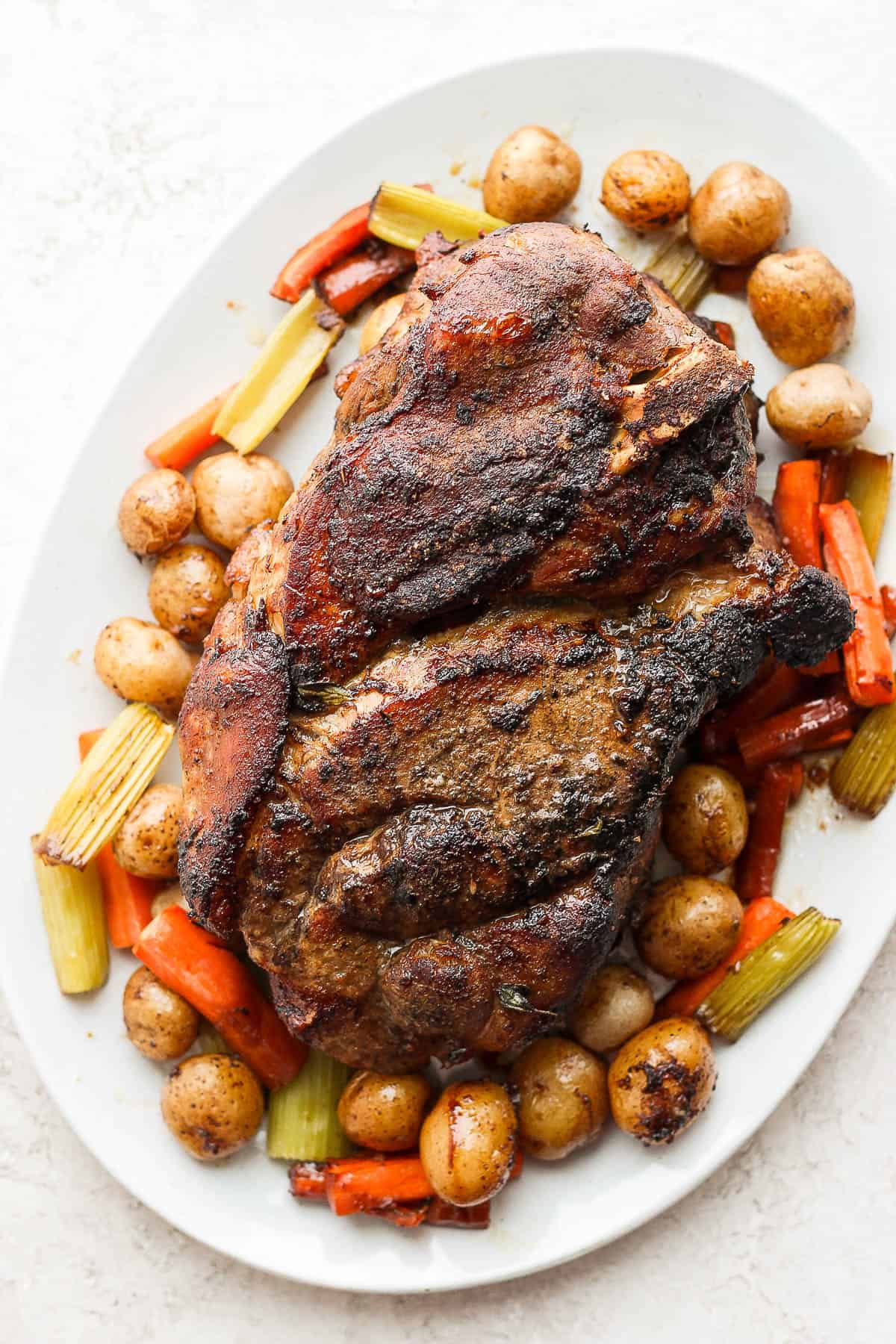 A pork roast recipe on a platter with veggies and potatoes around it. 