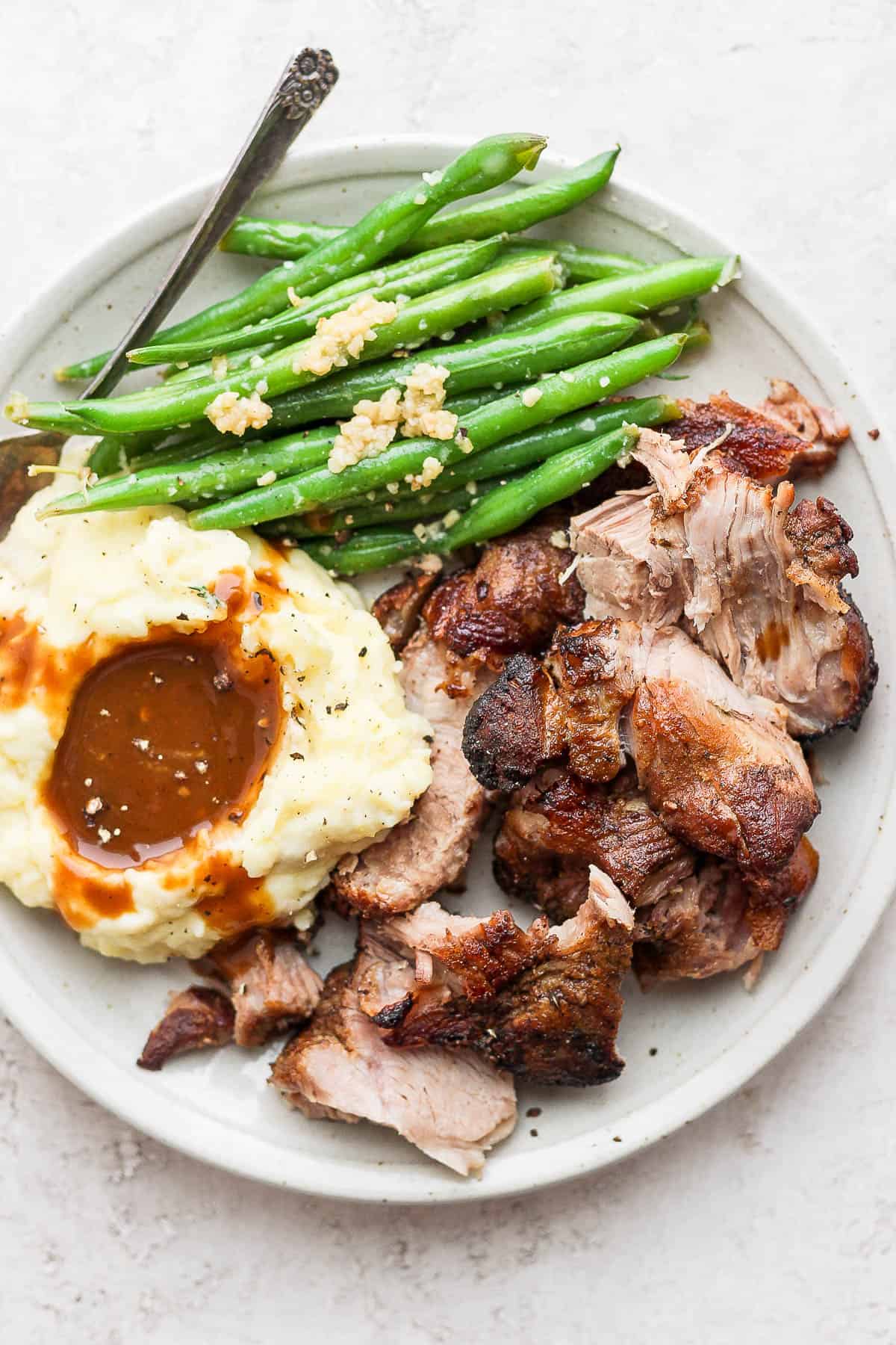 A plate of pulled pork, mashed potatoes and gravy and green beans. 
