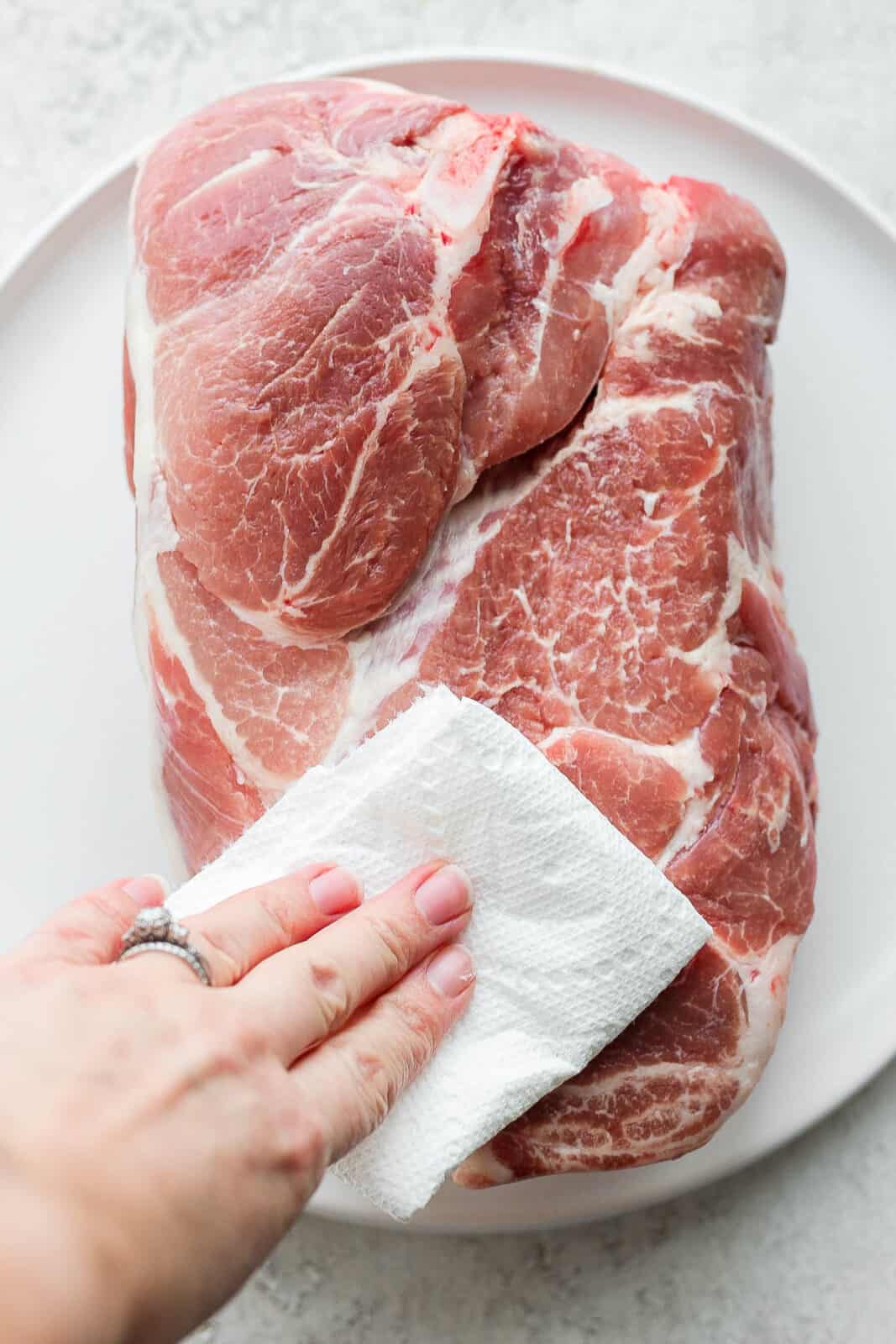 A raw pork roast on a plate with someone patting it dry with a clean paper towel. 