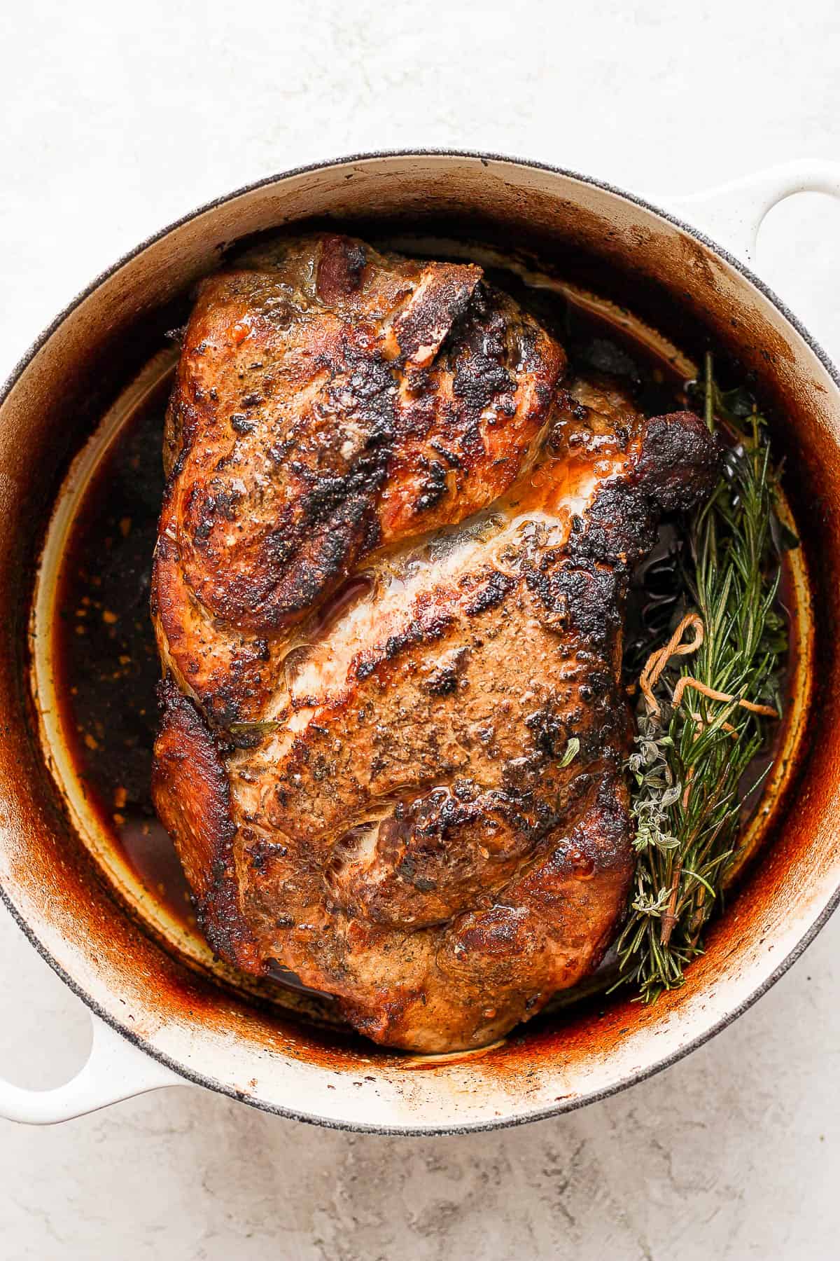 A pork roast recipe in a dutch oven with an herb bundle next to it. 