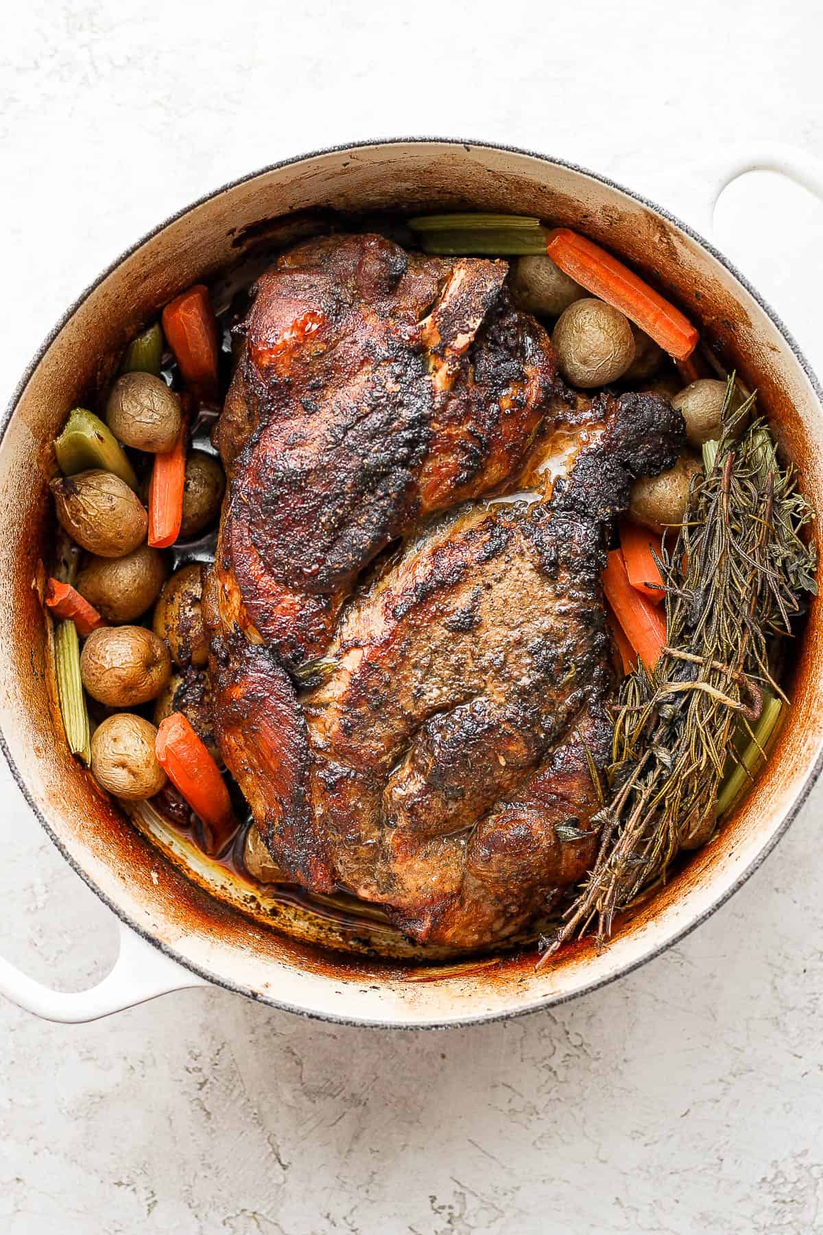 A fully cooked pork roast in a dutch oven with cooked veggies around it. 