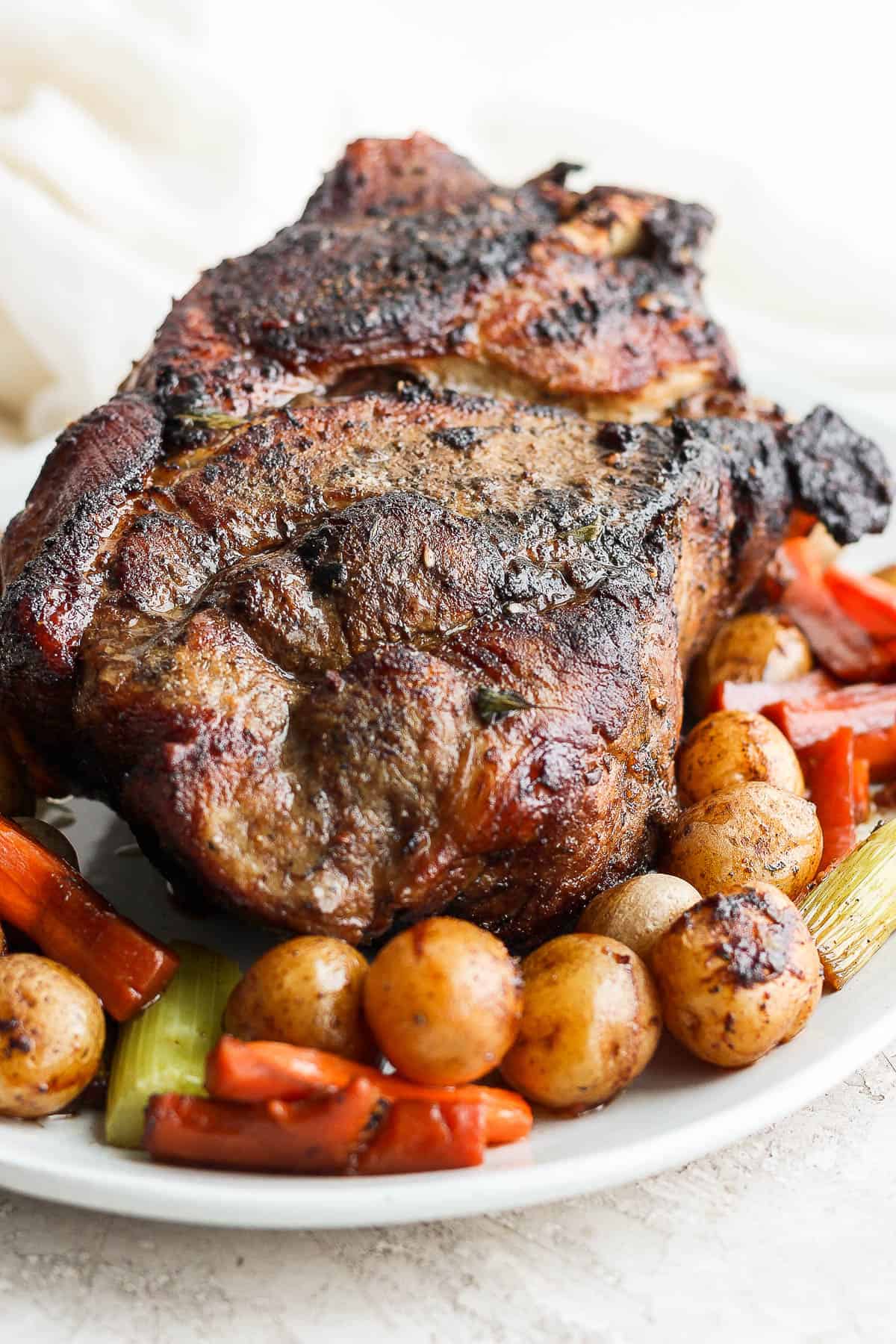 A pork roast on a platter with cooked veggies.