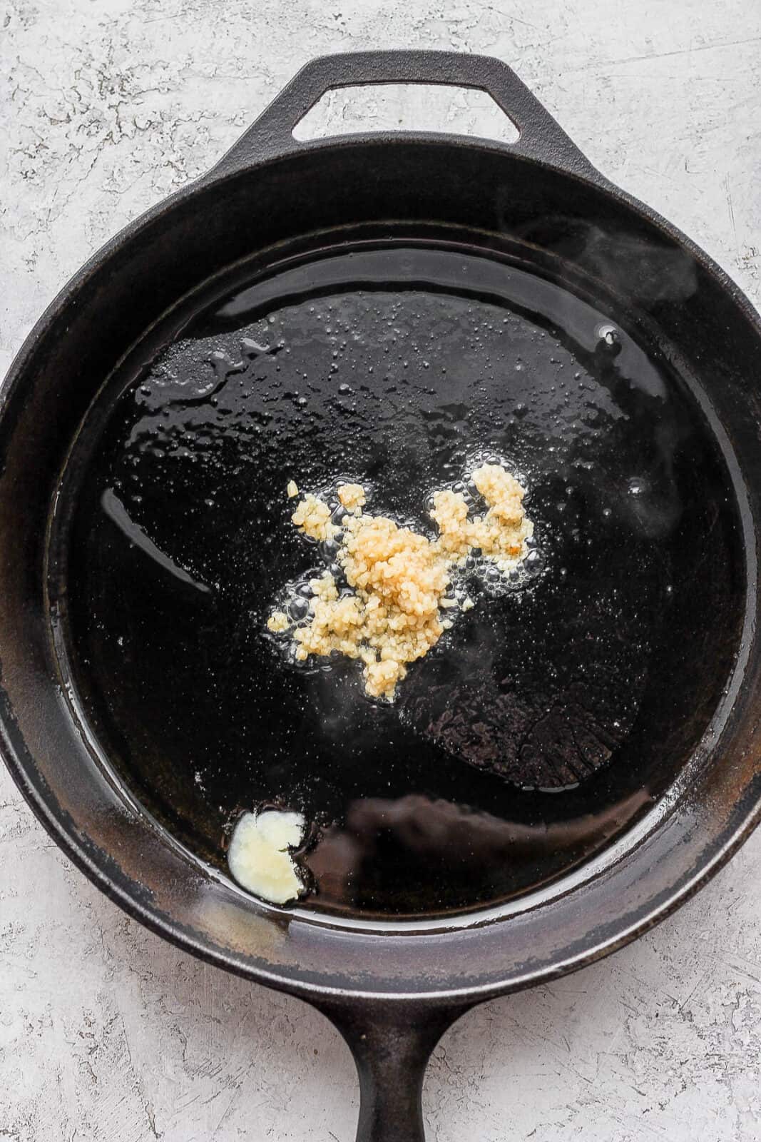 Ghee and garlic in a cast iron skillet.