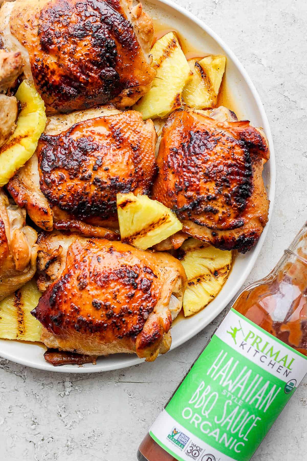 A plate of hawaiian chicken with grilled pineapple and a bottle of Primal Kitchen Hawaiian BBQ Sauce.