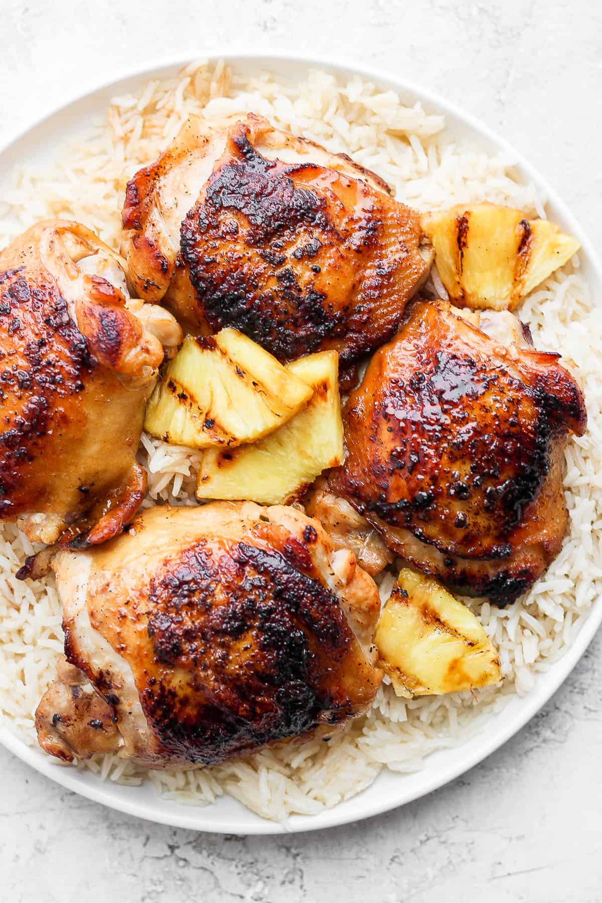A plate of Hawaiian Chicken on a bed of rice with grilled pineapple. 